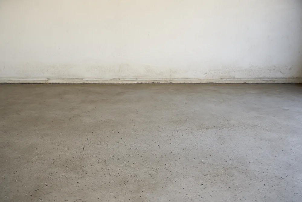 A concrete garage floor with a faint horizontal water mark along the base of the wall — garage floor coating, Bendigo. Illustrative example.